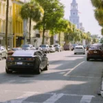 Charleston street lined with palm trees, parked cars, and a church steeple in the distance