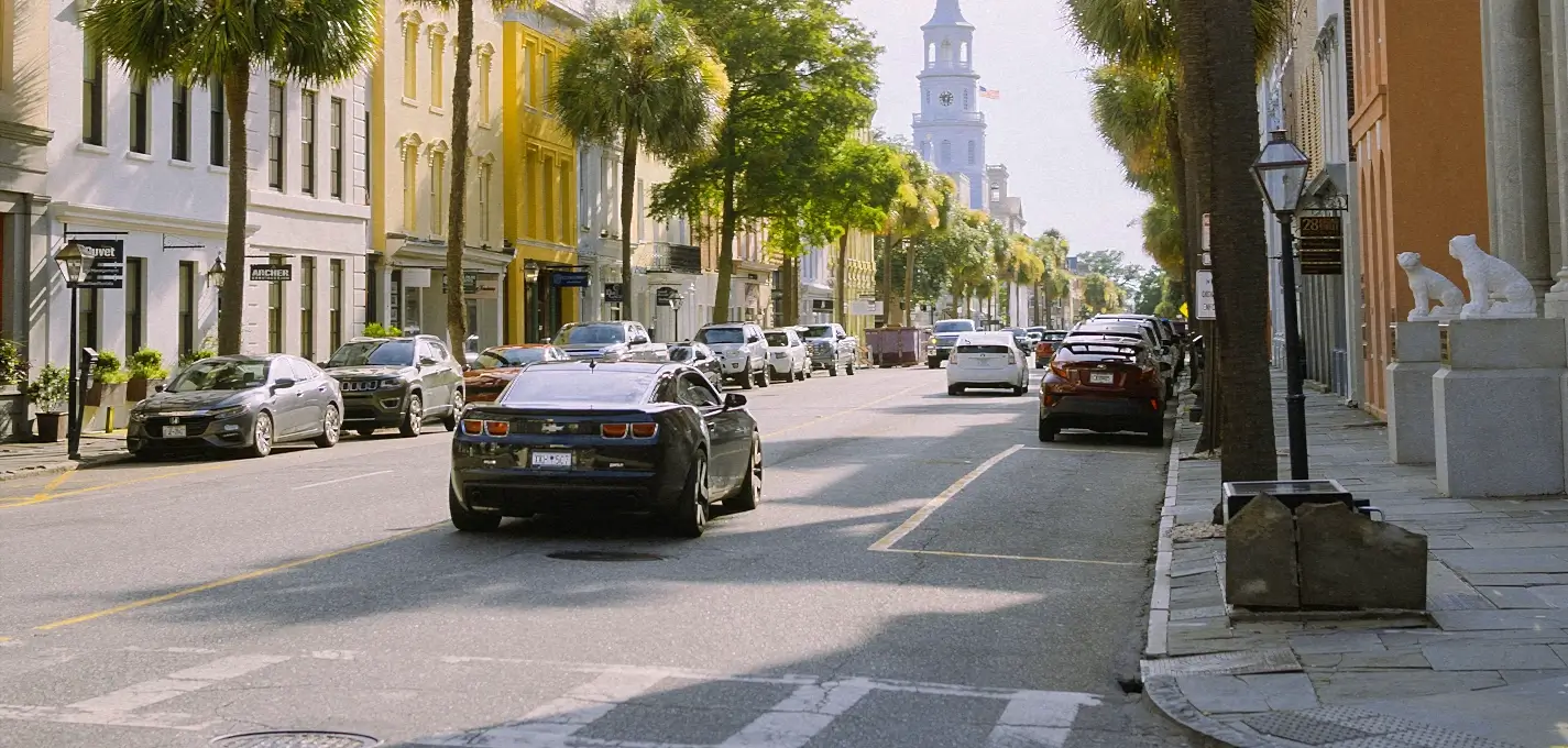 Charleston street lined with palm trees, parked cars, and a church steeple in the distance