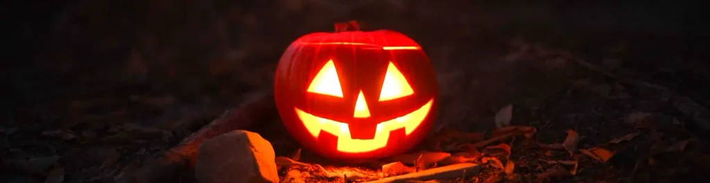 Classic carved pumpkin glowing warmly on a bed of autumn leaves and dirt at night, capturing the quiet outdoor Halloween atmosphere common along the Carolina coast.

