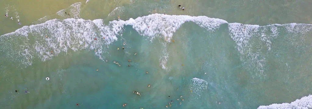 Aerial view of swimmers in the water among breaking waves at a crowded beach