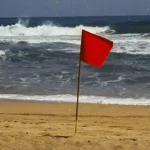 Red warning flag planted on the sand in front of breaking waves