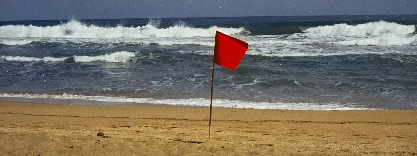 Red warning flag planted on the sand in front of breaking waves