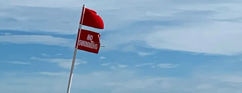 Red flag and 'No Swimming' warning flag on a beach flagpole
