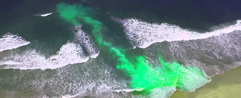 Aerial view of a green rip current channel pulling water offshore through breaking waves