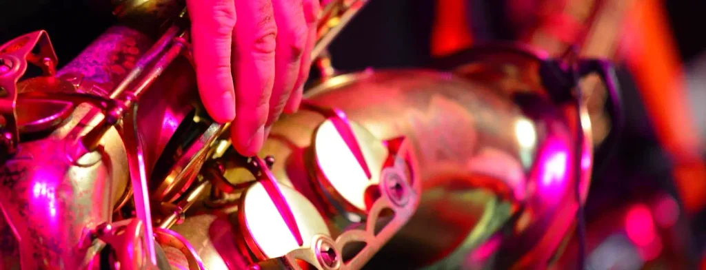 Musician's hand on saxophone keys bathed in pink stage lighting at Lowcountry Jazz Festival